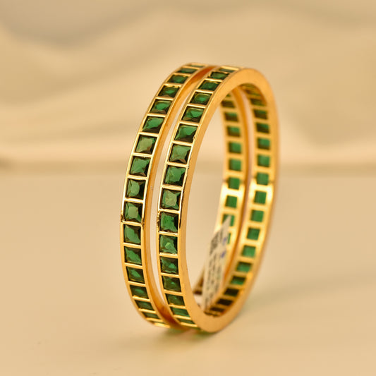 Gold polish ad bangle with square cut  emerald green color stones on a beige background
