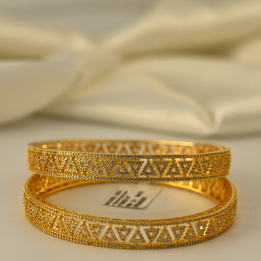 Two gold polish AD bangles with intricate designs on a beige fabric background