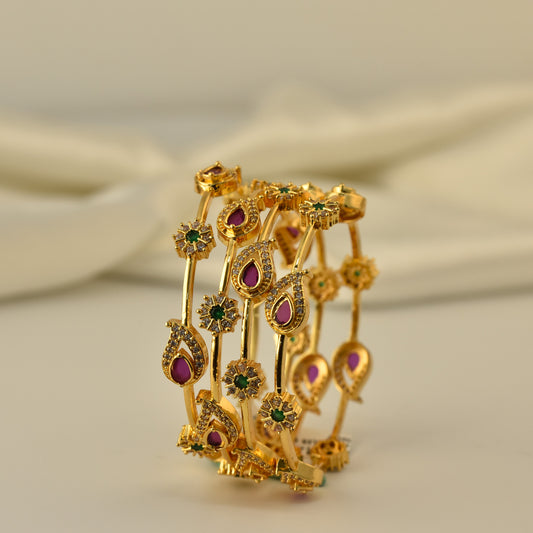 Gold polish 4pc bangle with red green and white stones in a mango shape motif on a beige background