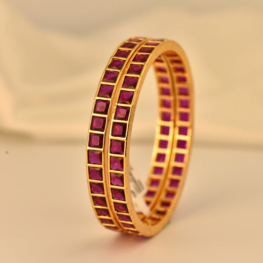 Gold polish ad bangle with square cut ruby like stone on a beige background