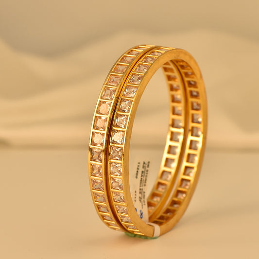 Gold polish ad bangle with square cut diamond-like stones on a beige background