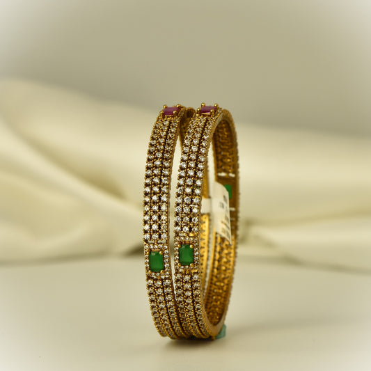 Antique Gold polish ad bangles with green ruby and white color stones on a beige fabric background