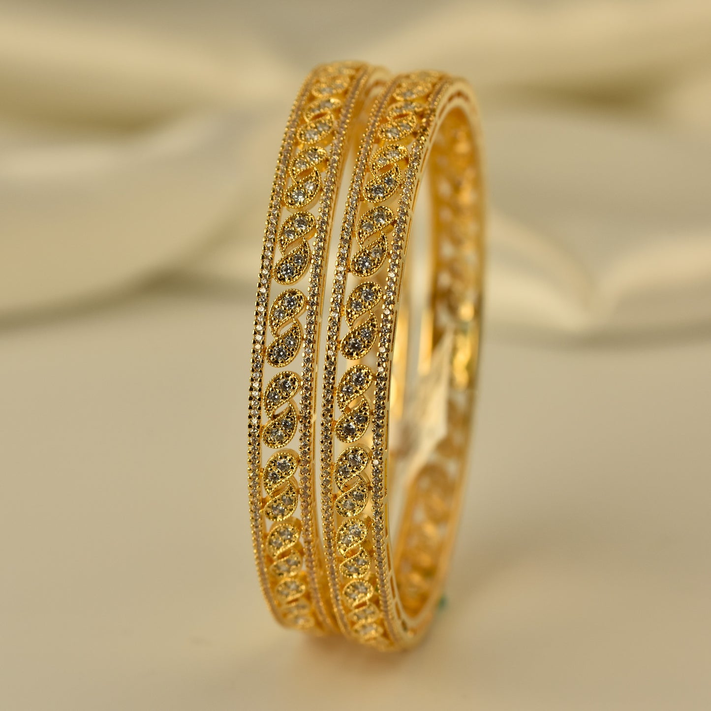 Gold polish ad bangle with white stone mango shape motif intricate design on a beige background