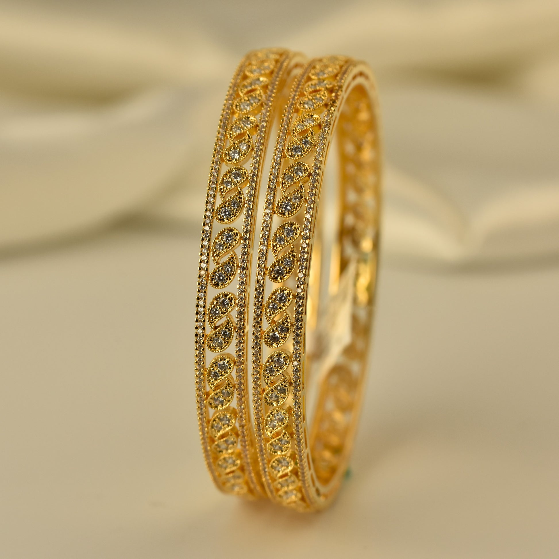Gold polish ad bangle with white stone mango shape motif intricate design on a beige background